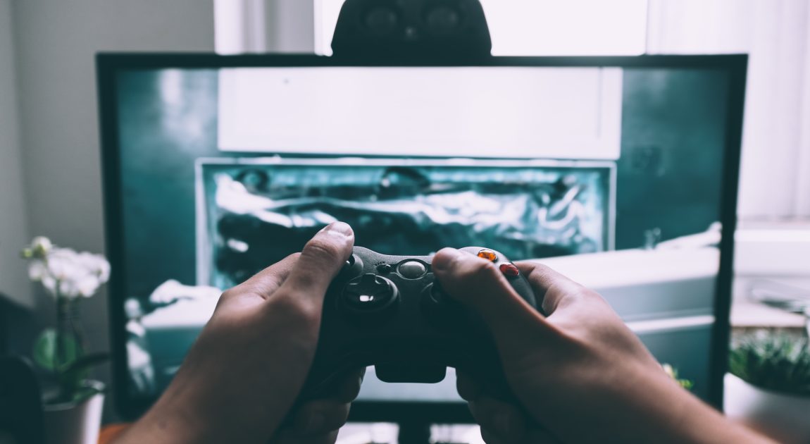 ディスプレイを前にコントローラーを操作する両手。株式会社CRI・ミドルウェアが独自の音声・映像技術「CRIWARE」を通じて、ゲーム開発の効率化と高品質化に貢献し、さらにモビリティやオンラインコミュニケーションなど新たな分野へ事業を拡大していることを示唆しています。