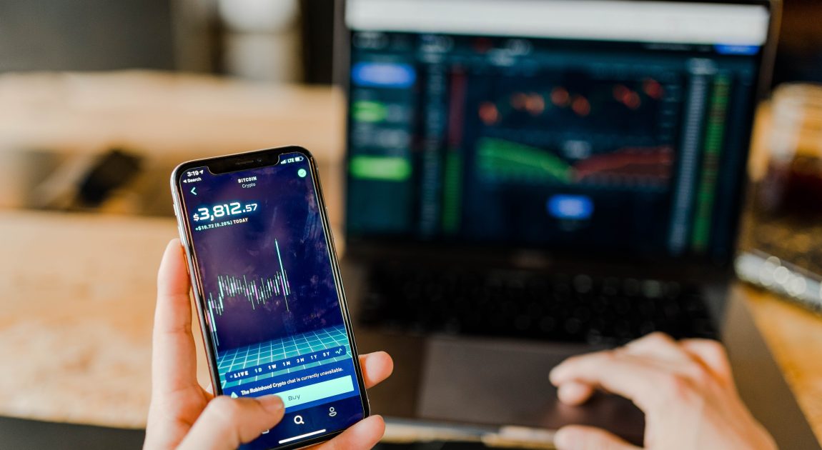 スマートフォンとノートパソコンに株価チャートが表示され、金融情報や投資ソリューションを提供する株式会社アイフィスジャパンのビジネスモデル「紙と電子の融合」を象徴する画像