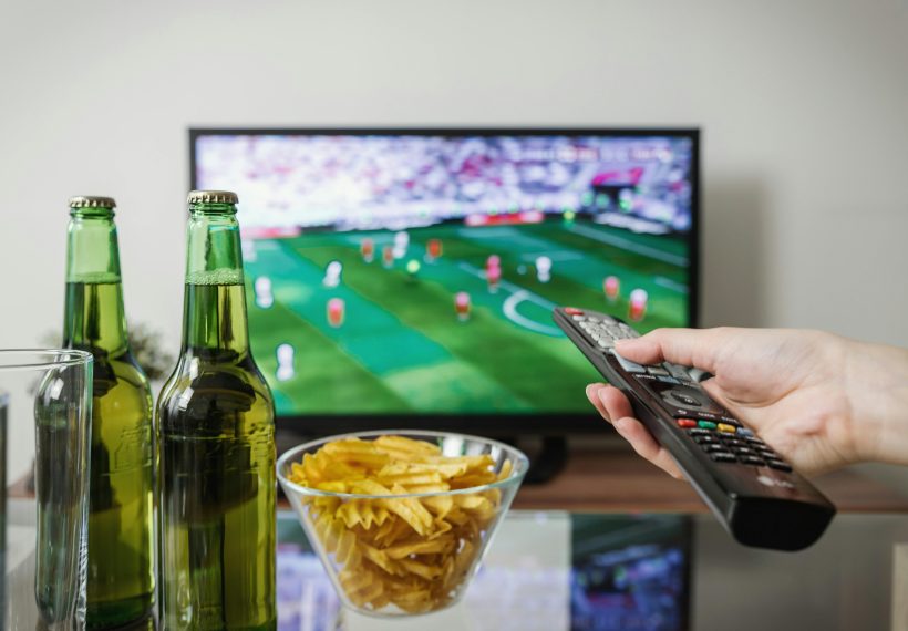 テレビを観ながら、手でリモコンを操作している様子。日本テレビホールディングスが、人気番組やコンテンツ配信を通じて国民生活を豊かにし、テレビ放送の枠を超えて多様なメディア・コンテンツ事業を展開していることを示唆している。