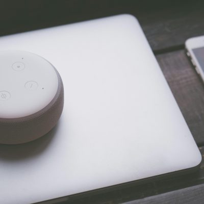 家電や電気設備などを幅広く取り扱うパナソニックホールディングス株式会社をご案内する記事に添える画像。リビングの木製テーブルに置かれたノートパソコンの上に、AI活用によるビジネス変革「Panasonic Go」を象徴するスマートスピーカーとスマートフォンが置かれている様子。