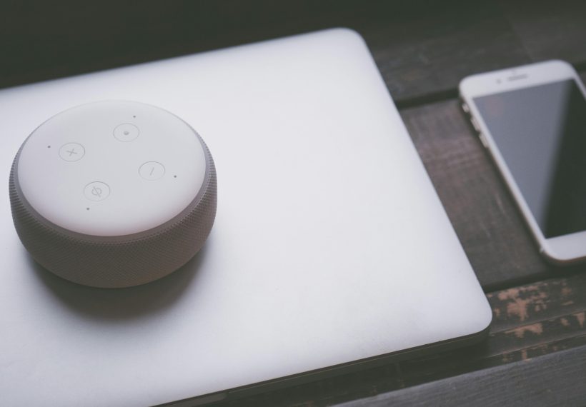 家電や電気設備などを幅広く取り扱うパナソニックホールディングス株式会社をご案内する記事に添える画像。リビングの木製テーブルに置かれたノートパソコンの上に、AI活用によるビジネス変革「Panasonic Go」を象徴するスマートスピーカーとスマートフォンが置かれている様子。